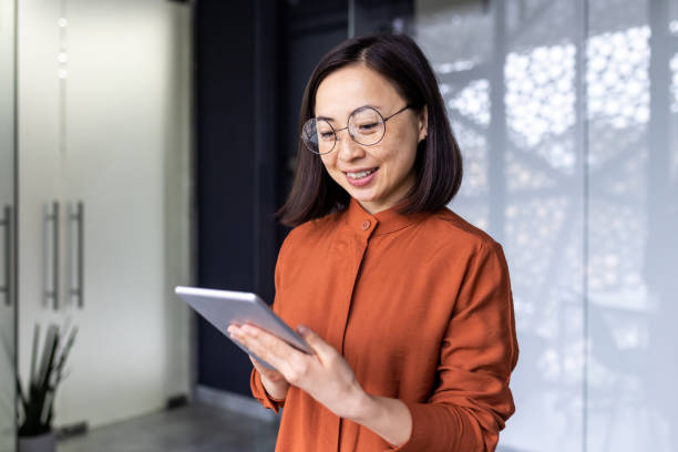 istock Smiling Asian young female programmer standing in office and working on tablet 1690939326