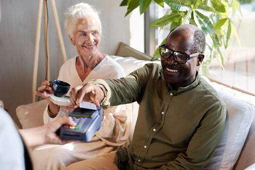 Smiling African American man paying for coffee with credit card while sitting in cafe with his wife