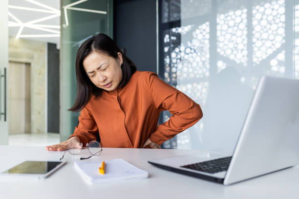 istock Tired woman at workplace, backache from sitting work, office worker massaging side of back overworked asian woman working at workplace inside modern office with laptop 1690941238
