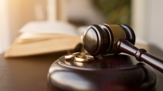 Judge gavel and wedding rings for divorce proceedings. Mallet of a judge deciding on marriage divorce case and custody. Selective focus on the rings.