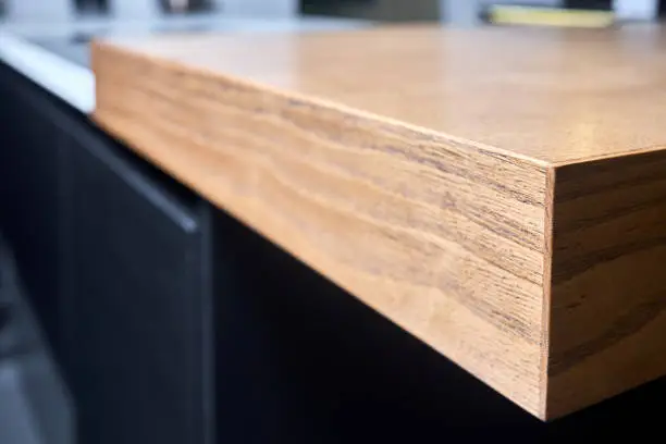 Solid ash glued timber under varnish edge corner table top selective focus macro closeup. Kitchen interior contemporary design countertop, tabletop.
