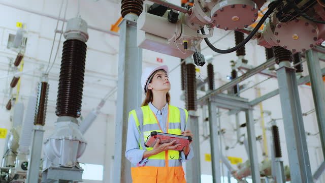 Female electrician checking electric voltage by tablet, recording electrical protection relay parameter in control room, electricity operator station in industry factory