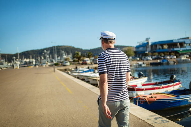 Mature man standing near the sea dressed in a sailor's shirt and hat.