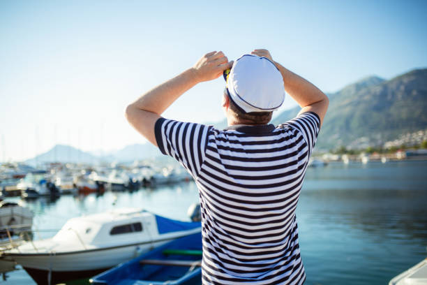 Mature man standing near the sea dressed in a sailor's shirt and hat.