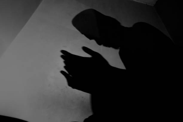 shadow of a Muslim man praying. Shadow on the wall of muslim man praying during prayer, muslim or islamic man sitting praying. i love allah in arabic silhouettes stock pictures, royalty-free photos & images