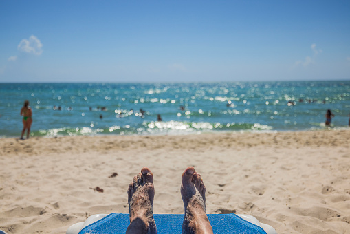 Close-up view of men's feet on sun bed in focus on blurred ocean water background. Miami Beach. USA.
