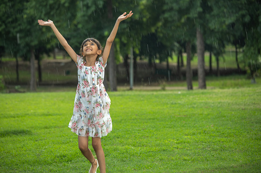 Carefree girl with arms raised enjoying rainfall while standing on grassy field in park