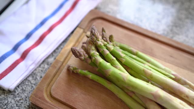 Asparagus shoots on wooden board in kitchen. Recipes with vegetables. Handheld, slow mo