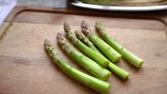 Six Asparagus shoots on wooden cutting board. Handheld, dolly, slow motion