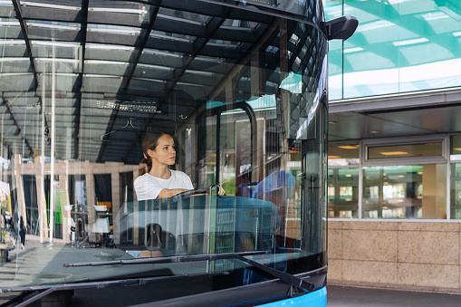 Young woman driving a shuttle bus at a suburban bus station, female shuttle bus driver occupation and employment.