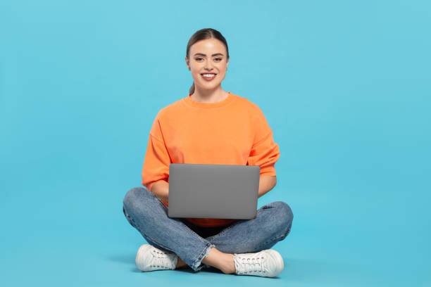 istock Happy woman in headphones using laptop on light blue background 1690992196