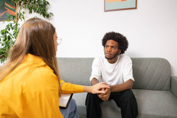 Unrecognizable female psychotherapist consoling her male patient Black ethnicity Caucasian female psychotherapist talking with male patient Black ethnicity during therapy session nervous holding hands stock pictures, royalty-free photos & images