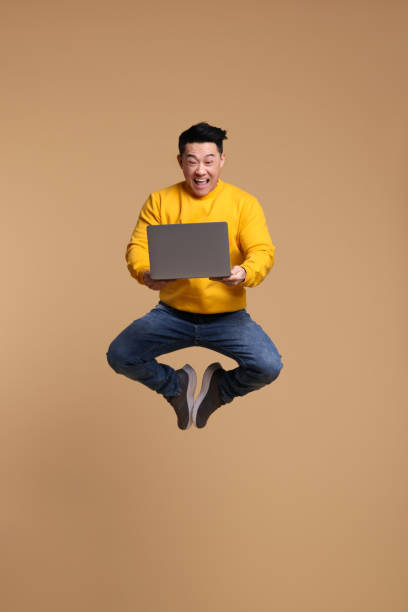 istock Happy man with laptop jumping on beige background 1690992304