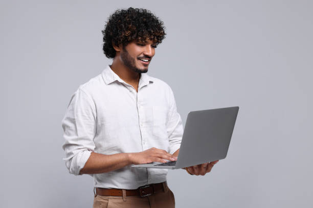 istock Smiling man with laptop on light grey background, space for text 1690992378