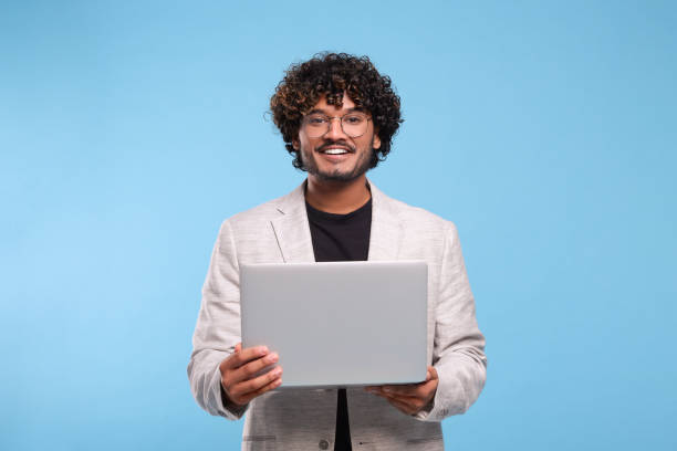 istock Smiling man with laptop on light blue background 1690992415