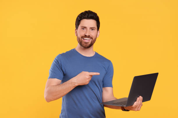 istock Happy man with laptop pointing at something on yellow background 1690992423