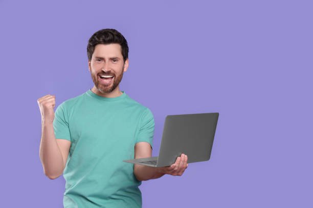 istock Emotional man with laptop on purple background. Space for text 1690992445