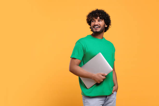 istock Smiling man with laptop on yellow background, space for text 1690992540