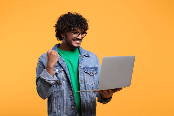 istock Happy man with laptop on yellow background, space for text 1690992554