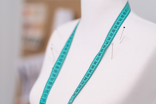 Mannequin with pins and green tape measure in sewing atelier professional dressmaker supplies for outfit making in craft fashion workshop bare dummy closeup