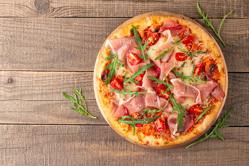 Pizza with prosciutto, ham, arugula, tomatoes, pesto, cheese and parmesan. Italian cuisine.