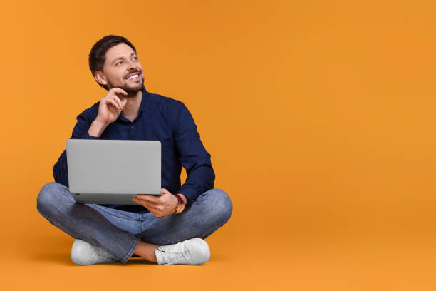 istock Happy man with laptop sitting on yellow background, space for text 1691000804