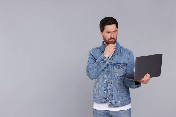 istock Confused man with laptop on light grey background. Space for text 1691014642