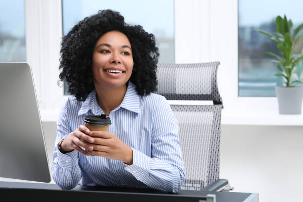 istock Young woman with cup of drink working on computer in office 1691035387
