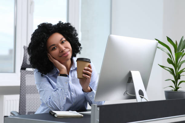 istock Young woman with cup of drink working on computer in office 1691035406