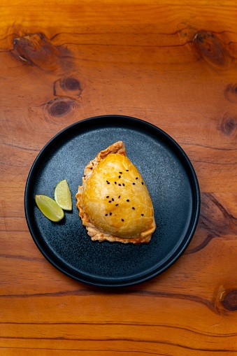 This is an image of a freshly cut slice of pie on a black plate, accompanied by a small wedge of lime, sitting atop a wooden table