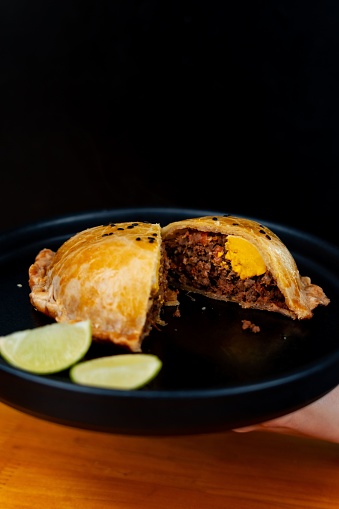 A person is carefully slicing a freshly-baked patty onto a plate, garnished with slices of lime