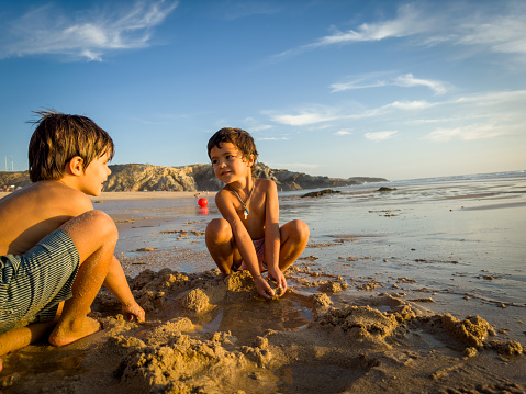 Two little friends play happily on the beach sand at the end of the day