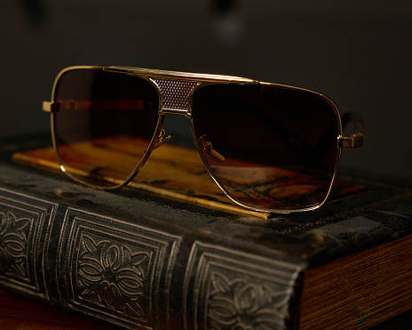 Gold trim squared aviator sunglasses with gradient brown color lenses sitting on antique book.