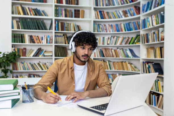 istock Serious concentrated man in headphones studying in library, hispanic student thinking and recording video course while sitting in university campus library 1691051813