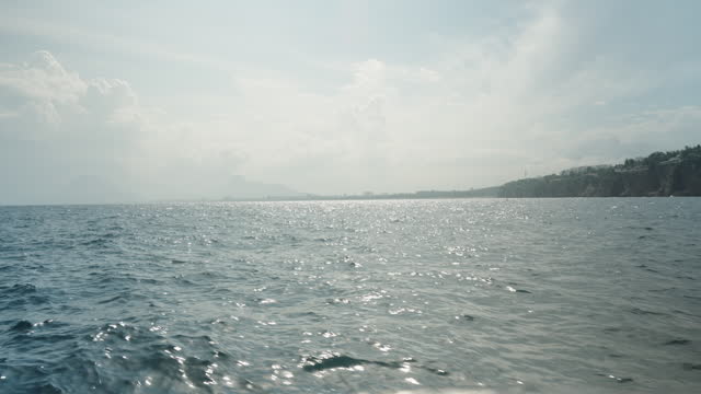 A sea excursion, view of the waves from the boat, a city in the distance on cliffs, sunny weather. Slow motion.