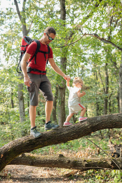 istock Young man hiking through forest with his daughter, crossing the fallen tree 1691055706