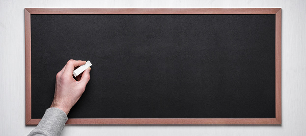 Hand holding chalk on blackboard. Male hand with chalk on the empty blackboard or chalkboard.