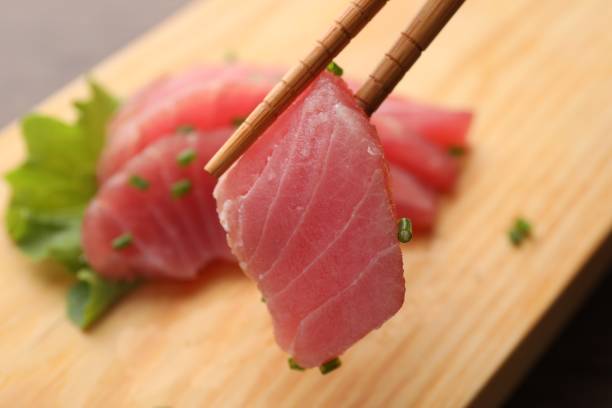 istock Holding tasty sashimi (piece of fresh raw tuna) with chopsticks against blurred background, closeup 1691066824