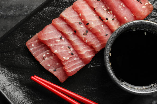 istock Tasty sashimi (pieces of fresh raw tuna with sesame seeds) and soy sauce on black plate, flat lay 1691067585