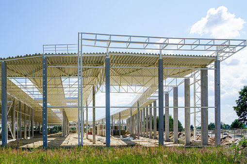 New unfinished large building steel framework with corrugated steel roof on reinforced concrete supports, blue sky background