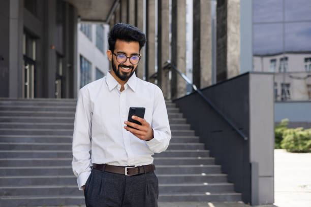 istock Closeup businessman walking city and using application on smartphone, a smiling Hispanic man holding a phone in his hands, browsing online pages, typing messages, and choosing in online store 1691078877
