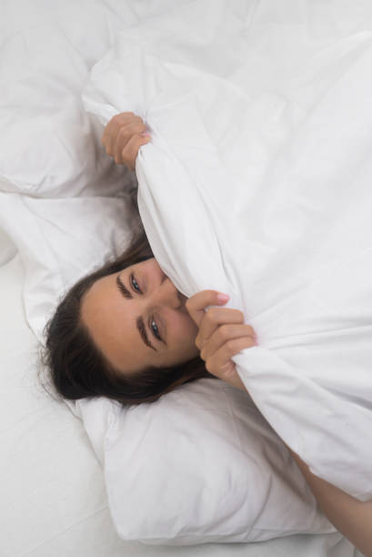 istock Morning joy: she grins, cocooned under a white blanket, savoring comfort in her bed's embrace 1691079420
