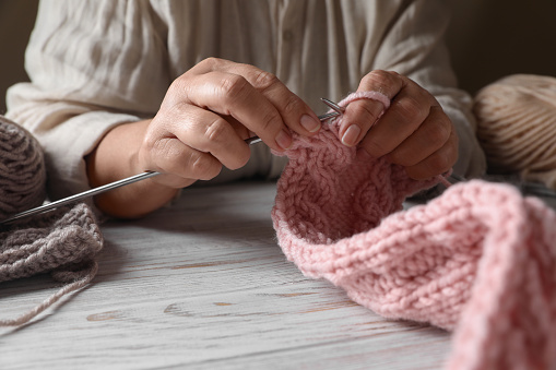 Woman knitting at white wooden table, closeup. Creative hobby