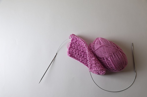 Knitting, needles and soft pink yarn on light background, top view. Space for text