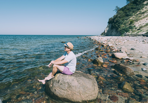 Man relaxes sitting  on stone with beach in background, Poland