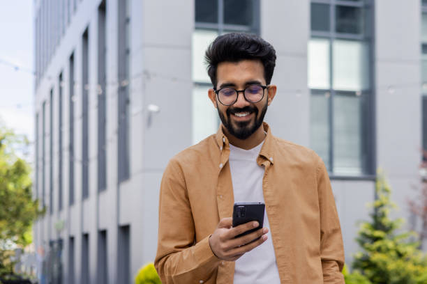 istock A young Hindu programmer engineer is walking outside an office building, a businessman is holding a phone and typing a message, a man in a shirt and glasses is smiling and browsing social media 1691100124