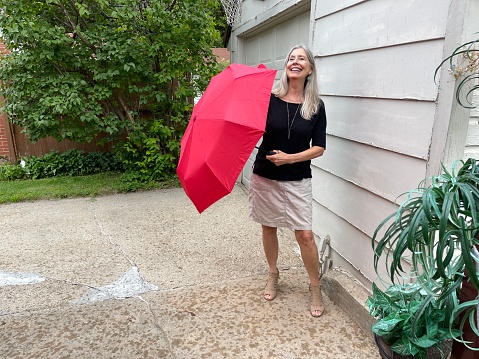 Active senior woman having fun as she holds an open red umbrella outdoors