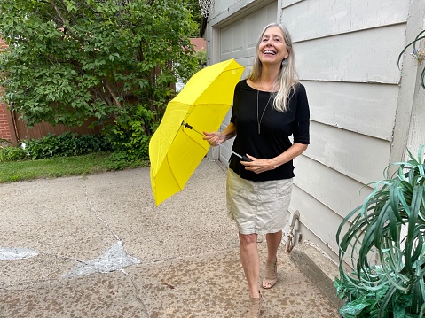 Active senior woman smiling as she holds an open yellow umbrella outdoors