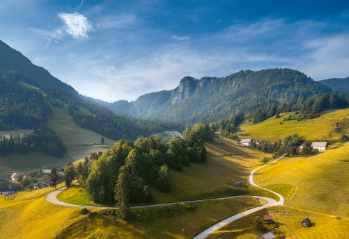 Aerial view of green hills with long winding country road at sunset in summer. Top drone view of Alpine mountains, green grass, blue sky with clouds. Slovenia