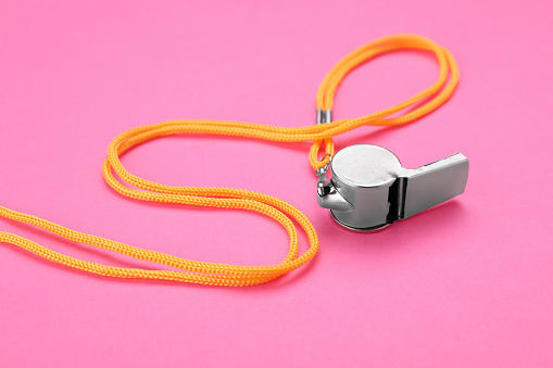 One metal whistle with cord on pink background